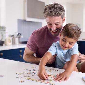  Imagem de pai e filho montando um quebra-cabeça. Ao fundo, uma cozinha com armários na cor azul e bancada branca.