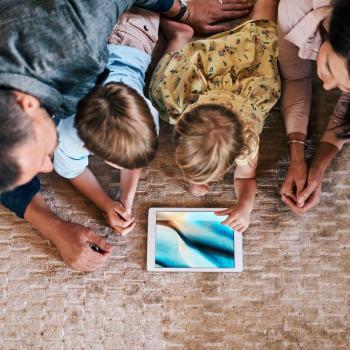 Tempo de tela: pai, mãe e duas crianças pequenas estão deitados em um tapete e olham juntos para a tela de um tablet.