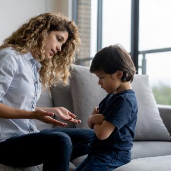 Uma mãe está sentada em um sofá e conversa com seu filho, representando como dizer não. O filho está em sua frente, com braços fechados e rosto de insatisfação. 