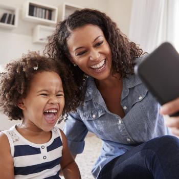 Sentadas no chão, mãe e filha sorriem ao tirar uma foto com o celular. As duas apresentam uma personalidade parecida.