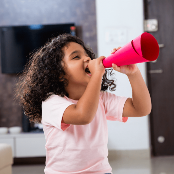 Menina sorri enquanto grita algo utilizando um megafone feito de papel enrolado, ilustrando a hiperatividade.