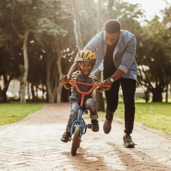 Para criar boas lembranças, pai ensina filho a andar de bicicleta em um parque.