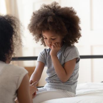 Para ilustrar a depressão infantil na foto, mãe consola a filha, que está sentada, com expressão triste, em cima da cama.