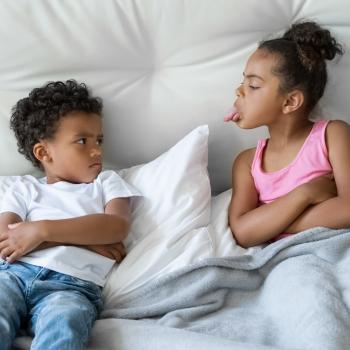 Dois pequenos irmãos brigando no sofá de casa.