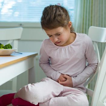 Menina com intoxicação alimentar, sentada à mesa de jantar, reagindo à dor, colocando as mãos na barriga. 