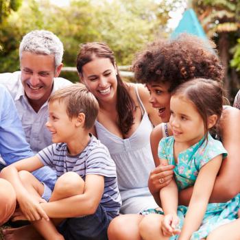 Uma família composta pela dinâmica da multiparentalidade conversa sentada na grama, em um parque