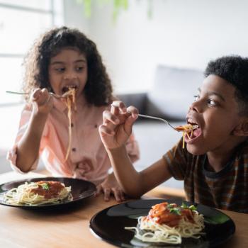 irmãos à mesa, comendo e se olhando na sala de casa