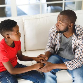 pai e filho sentados no sofá da sala de mãos dadas se olhando e conversando com expressões sérias