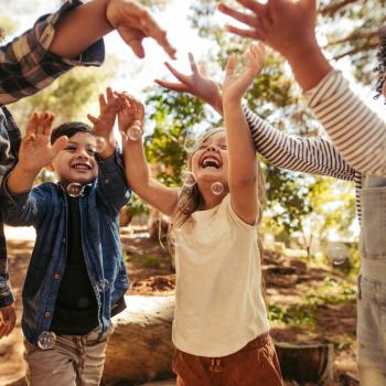 Crianças sorridentes num parque, brincando ao ar livre com bolhas de sabão