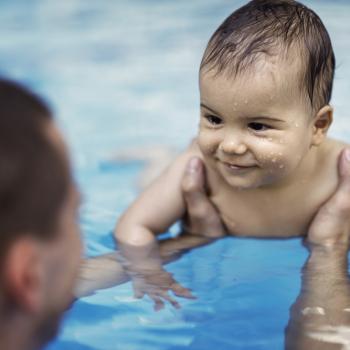 Homem segurando bebê sorridente na piscina.