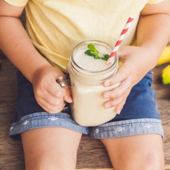 criança sentada ao redor de algumas bananas, segurando vitamina