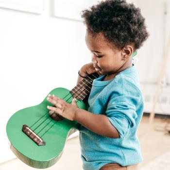 Menino com um violão na mão tentando tocar