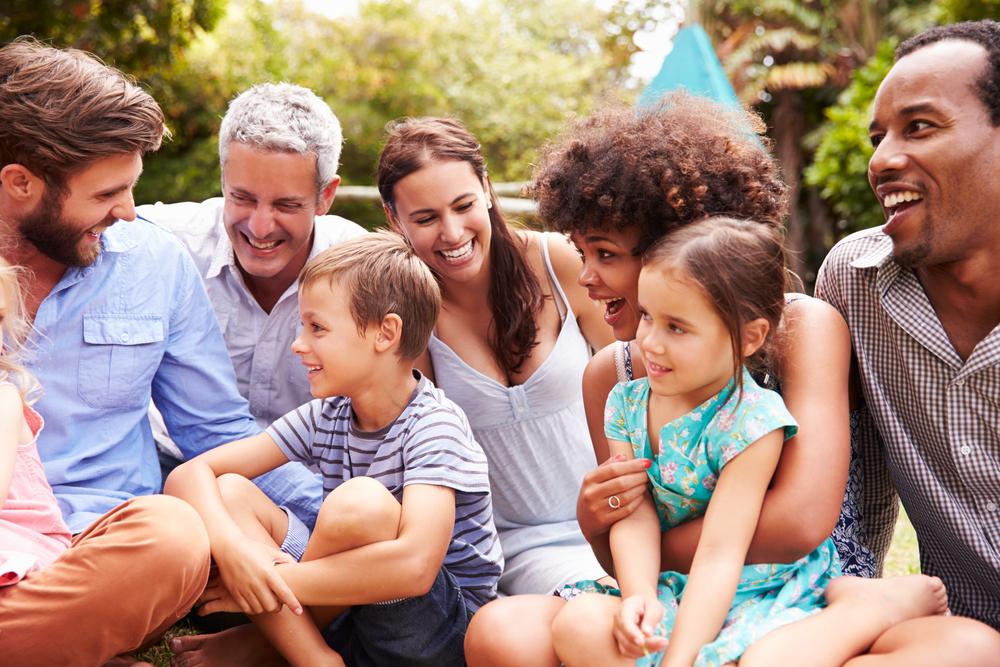 Uma família composta pela dinâmica da multiparentalidade conversa sentada na grama, em um parque