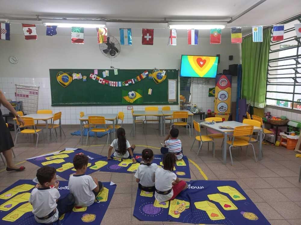 Crianças sentadas numa sala de aula assistindo a televisão 